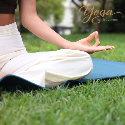 Person meditating in lotus position on a blue yoga mat in a lush green garden