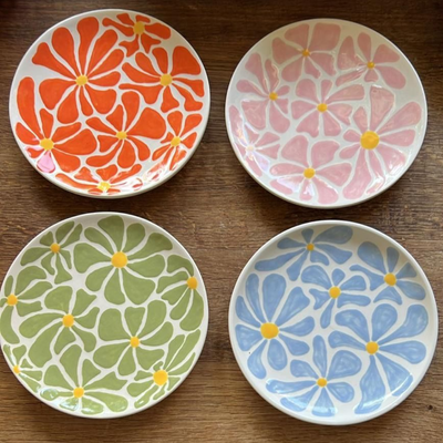 Four hand-painted ceramic plates with bright floral designs in orange, pink, green, and blue