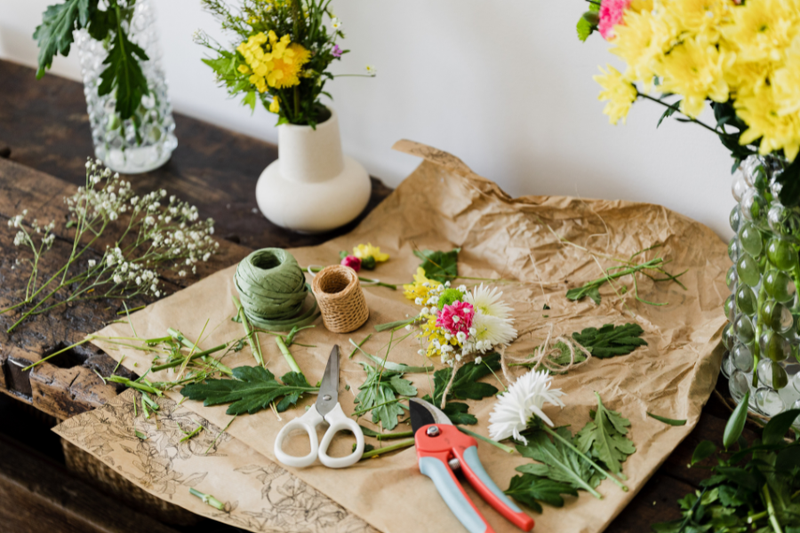 Floral arrangement workspace with scissors, twine, and fresh flowers on brown craft paper