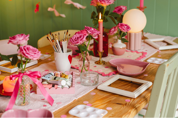 Beautifully styled party table with pink roses, candles, paintbrushes, and craft supplies